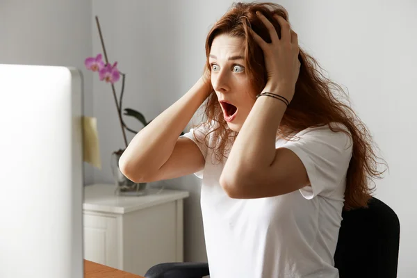 Shocked female office worker having unsaved data problem on laptop while working in the office. Young woman freelancer looking in horror at the computer screen with hands on head and wide open mouth