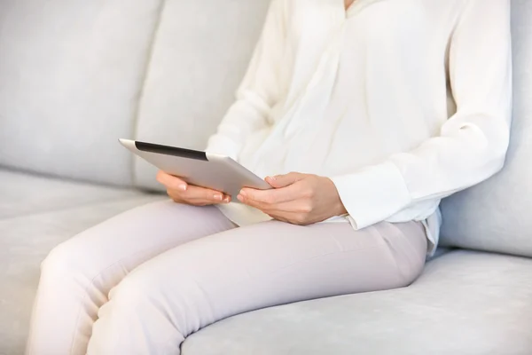 Cropped portrait of housewife wearing casual clothes sitting on sofa and holding electronic gadget while ordering food delivery online. Young woman reading news or checking email on her digital tablet