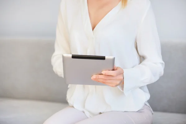 Cropped shot of woman using digital tablet, sitting on the sofa. Female entrepreneur checking email and reading news on electronic device in the morning before going to the office.  Selective foucs
