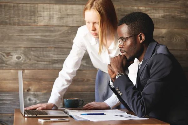 Business and career concept. Teamwork and cooperation: African man in formal suit and Caucasian woman in white shirt videoconferencing and negotiating with their partners using generic laptop