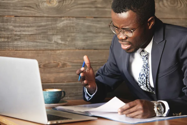 Disappointed African businessman is dazed and confused by a mistake in official documents. His bewilderment makes his eyebrows frowned and face unhappy. He feels total disagreement about the deal.