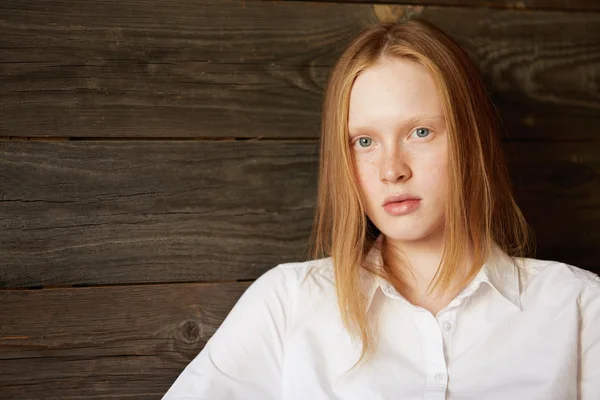Full face beautiful portrait of beautiful and young Caucasian girl on wooden background. Blond office woman in white shirt staring attentively at camera with relaxed face and peaceful emotions.