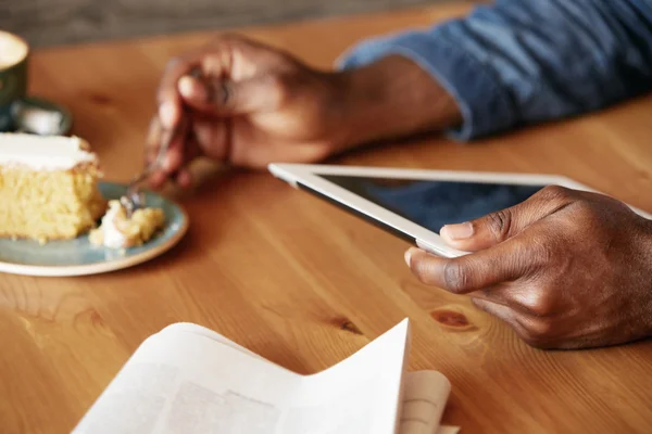 African student spending morning at a cozy cafe, having breakfast, reading e-book or texting with friends using digital tablet with copy space screen for your information. Selective focus on the hand