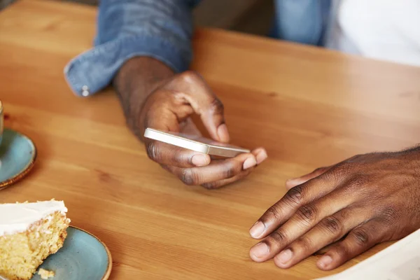 Film effect. Close up shot of African man\'s hands holding mobile phone while using wireless high-speed Internet connection. Black student texting friends via social networks sitting at a coffee shop