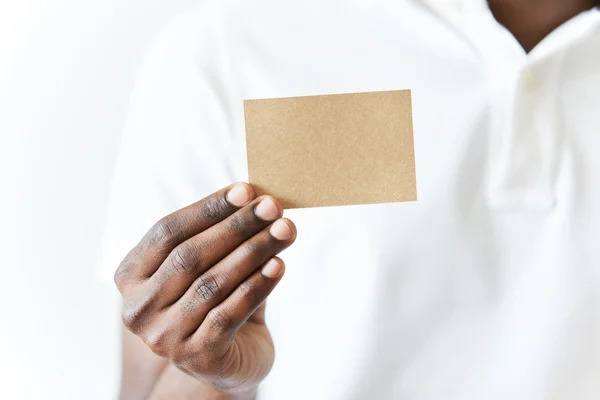 Close up of African man's hands holding business card with copy space for your text or advertising content. Black male wearing white polo shirt showing blank parchment card at the camera. Film effect