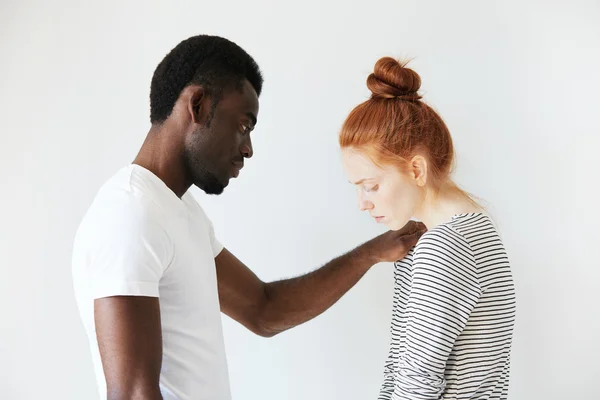 A touching scene of African American man comforting young redhead girl. He put his arm on her shoulder to sympathize her failure and to support her in hard times. Caucasian girl looks down in sorrow.