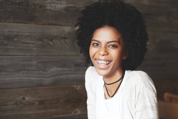 Human face expressions and emotions. Young attractive and charming black woman laughing sincerely at a funny joke, looking at the camera, against wooden wall background, wearing black choker necklace