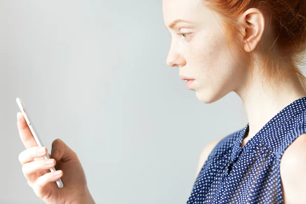 Crop profile portrait of young girl with ginger hair, holding a web-enabled mobile phone with malfunction, trying to reload it, pushing key of touch screen, having serious worrying face expression