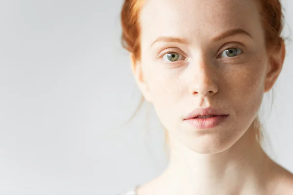 Skin care and beauty concept. Highly-detailed portrait of the face of pretty redhead female with pure healthy ideal skin with freckles looking at the camera with a faint smile and with parted lips