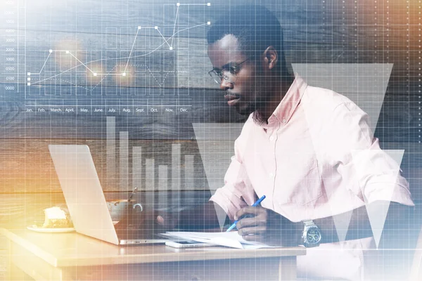 Double exposure of African American writer dressed in pink shirt using laptop writing an article for a newspaper with concentrated thoughtful expression sitting at a coffee shop against wooden wall