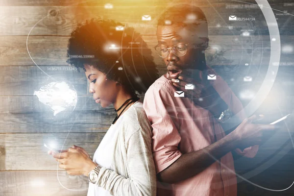 Double exposure of surprised jealous African man looking over his shoulder, watching his stylish African wife texting someone standing back to back, suspicious of her cheating on him. Visual effects