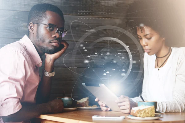 Double exposure of young African couple sitting at a cafe, man looking sad, bored, frustrated and offended, while his phone addicted girlfriend surfing the Internet on mobile phone with happy smile