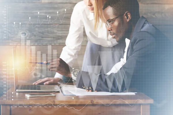 Corporate workers using brainstorm to find a new business solution: young African man pointing at the laptop screen with a pen, explaining something to his Caucasian female colleague. Visual effects