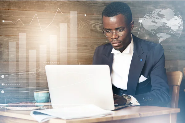 Career and success concept. Worldwide connection interface. Smart dark-skinned corporate worker in elegant suit and glasses working on generic laptop with copy space for your promotional content