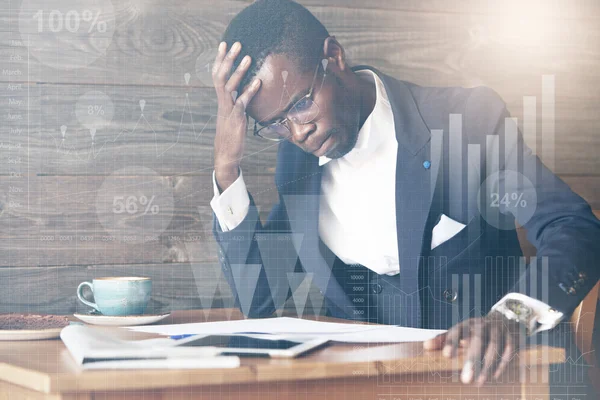 Double exposure of black corporate worker in glasses, looking worried and concerned about making a mistake in financial documents, holding his head, pursuing his lips, using copy space laptop