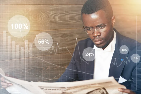 Visual effects. African American businessman wearing formal suit and glasses, reading financial newspaper with serious concentrated expression while waiting for his business partner at a hotel lobby