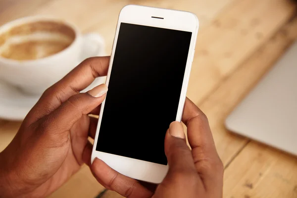 Close up of black woman's hands holding smart phone with blank copy space for your advertising content or promotional information. Female downloading updates on her mobile phone, sitting at a cafe