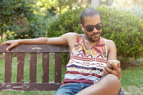 African guy in earphones sitting on bench