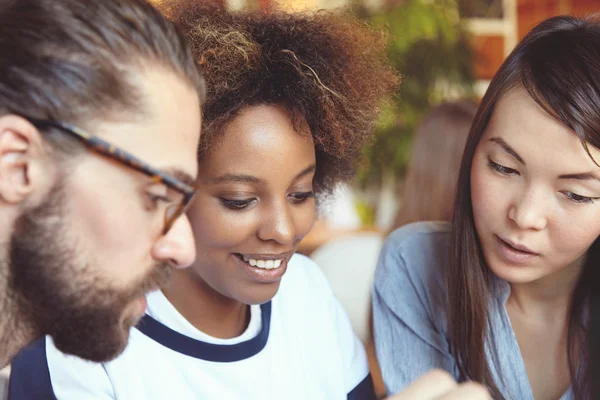 Cropped shot of young good-looking people. Caucasian man in glasses together with African and Asian girls studying something or reading useful information, having interesting and nice conversation