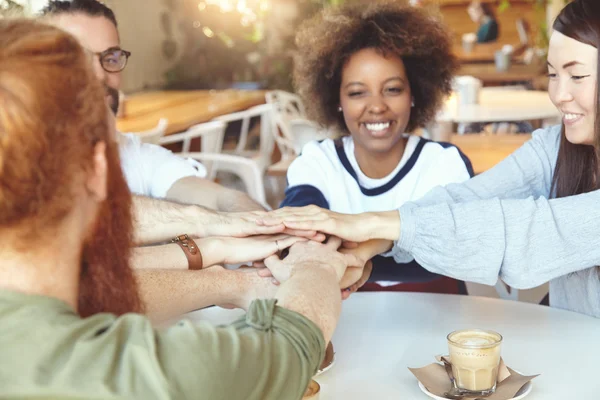 Friendship and communication concept. Group of young trendy students at coffee shop sitting at table with hands on top of each other, showing their unity and togetherness or making verbal agreement