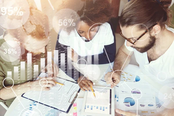 Visual effects. Top view of business partners discussing growth, making research, analyzing financial statistics and data of their start-up. Young people working with charts and diagrams using tablet