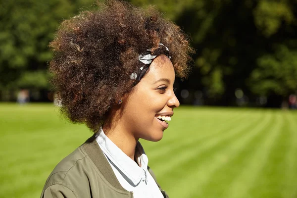 Profile of cute African student girl having short walk in city park on her way home from university. Young black female enjoying nice weather on sunny day outdoors, meeting her friends in urban forest