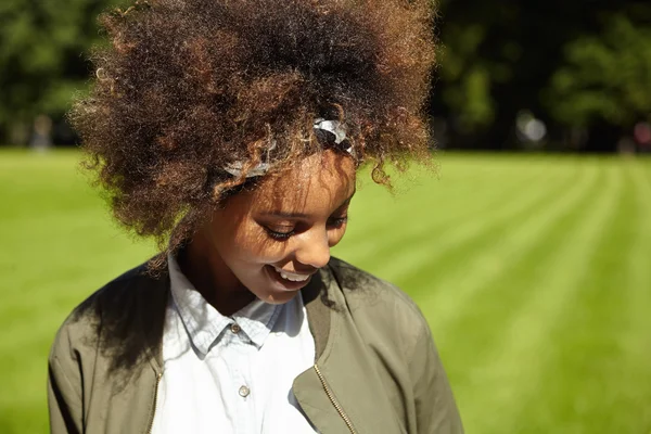 People and nature. Outdoor shot of hipster African woman in bandana, walking in city park, enjoying sunny weather, looking down with happy carefree smile. Black girl spending day-off in open air