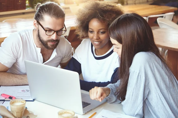 Brainstorm concept. Multiethnic group working at cafeteria, developing business strategy using laptop computer, looking concentrated. African girl showing presentaion to her partners on notebook