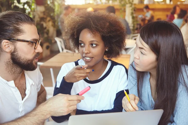 Brainstorm concept. Man in glasses explaining ideas and vision to his female partners while having hot dispute on common project. Multhiethnic team discussing business plans at coworking cafe