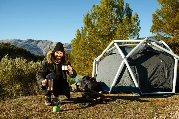 Man camping drinking coffee near tent smiling happy outdoors in