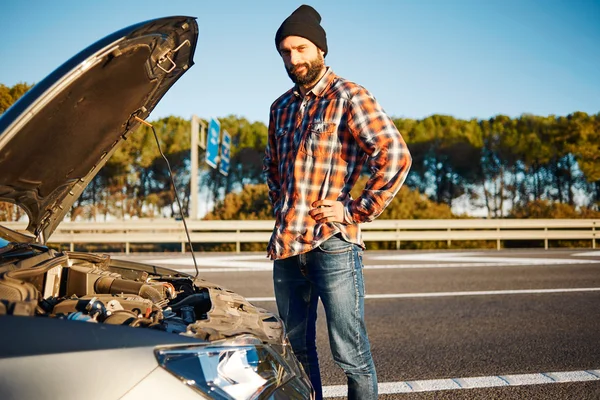 Car - young male model stands a careful look face and looking at camera on road trip at summertime. Transportation and vehicle concept - brutal man opening car bonnet on freeway going to sea in Spain.