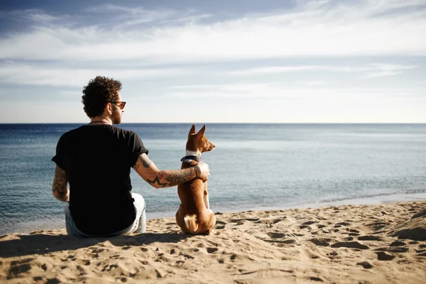 Caucasian man in sunglasses sitting in beach with friends dog