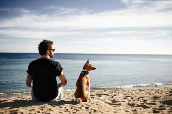 Caucasian man in sunglasses sitting in beach with friends dog