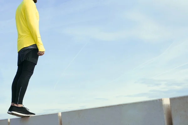 Sportsman in yellow wind breaker taking break with crossed hands standing on sky background. Fit man resting after workout outdoors, runner resting after fitness training.