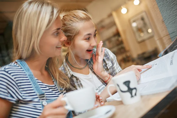 Two attractive young women reading magazine and wonder sitting i