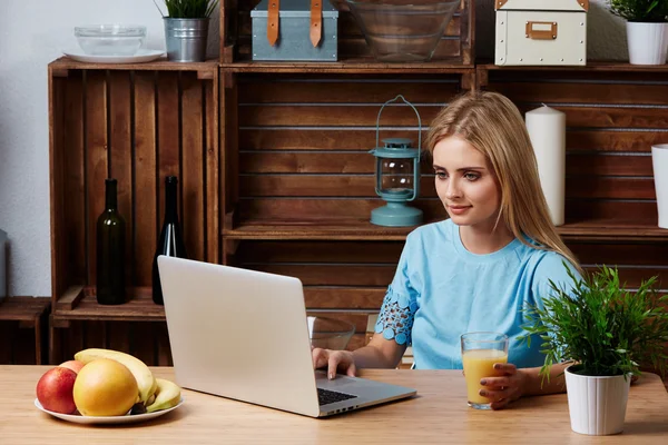 Young blonde woman looking for a recipe information on laptop computer in the home kitchen. Dieting Concept.