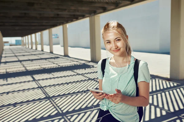 Portrait of young fitness asian girl in sportswear listening music with headphones after training outdoors at beautiful sunny day. Woman runner enjoying sun and listen music in earphones from tablet.
