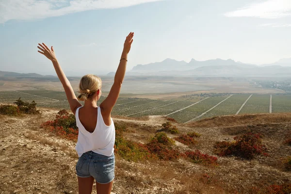 Happy celebrating winning success woman at sunset or sunrise standing elated with arms raised up above her head in celebration of having reached mountain top summit goal during hiking travel trek.