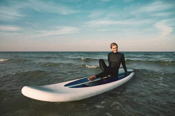 Beautiful young woman surfing lies on stand up paddle board at e