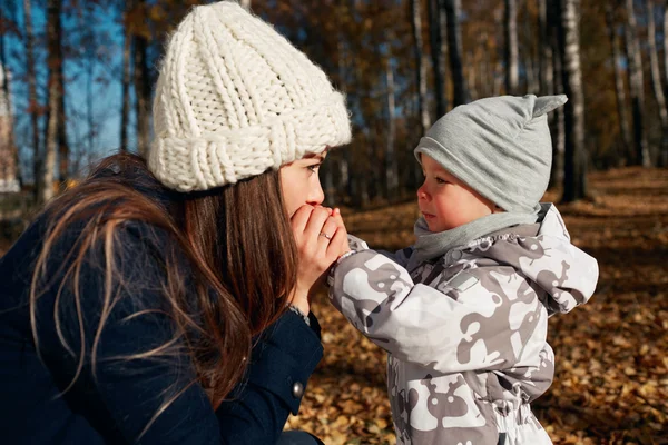 Attractive young mom and son looking on each other. Portrait of a happy mother and baby. Mother with her son worms his arms outdooe in autumn park