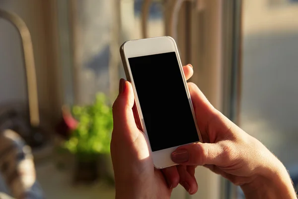 Woman hands holding a smart phone at home with a windows background.