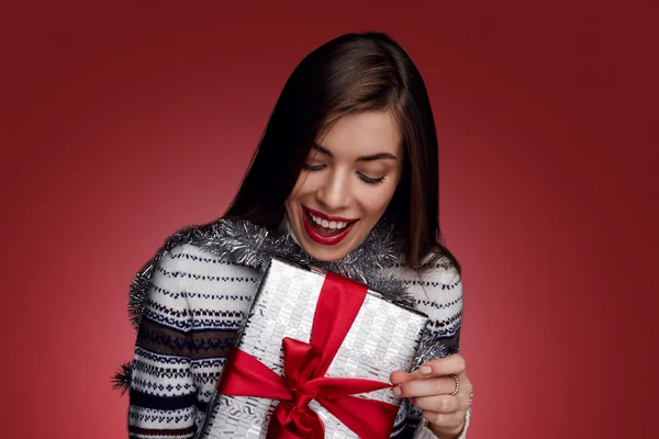 Portrait of happy woman opening gift box against red background.