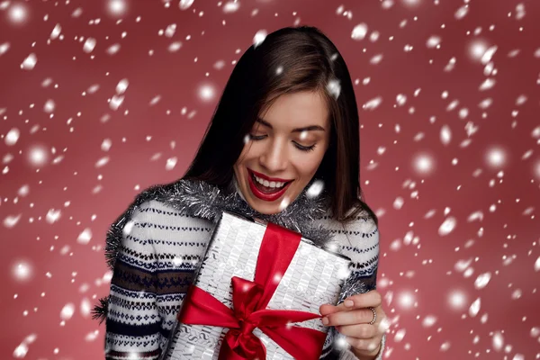 Portrait of happy woman opening gift box against red background.