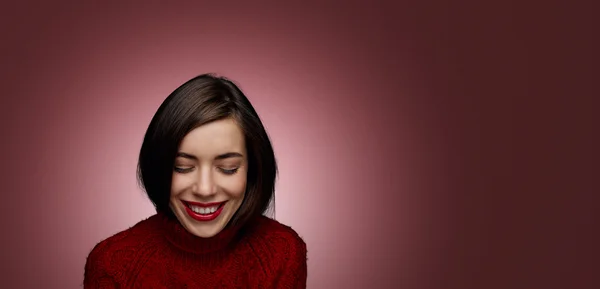 Woman with beauty brown hair, red lips and sweater- posing at studio.  Funny laughing surprised woman portrait with open mouth and sweet smile.