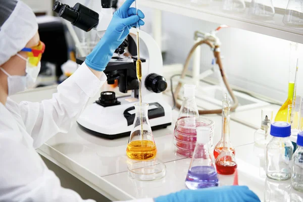 Science, chemistry, technology, biology and people concept - young female scientist mixing reagents from glass flasks and making test or research in clinical laboratory.