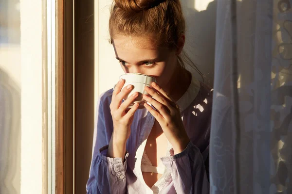 Beautiful woman drinking coffee in the morning sitting by the window.