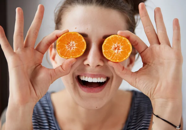 Young brunette woman holding tangerines instead of eyes, laughs and enjoys life. Harsh processing to emphasize the face structure. Human face expression body language reaction.