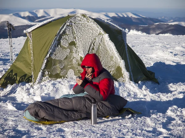 A man sits in a sleeping bag near the tent.