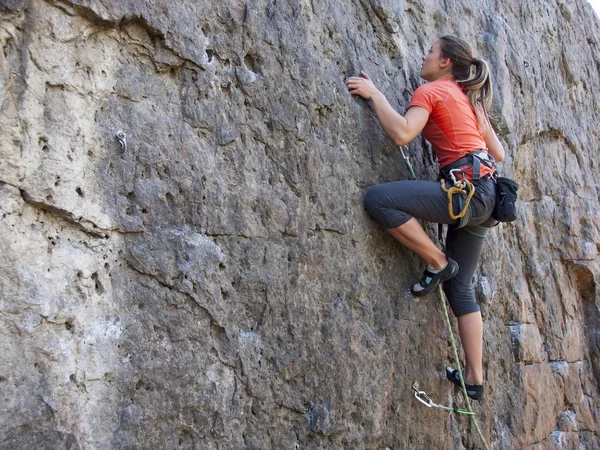 Young woman with rope climbs on the rock.