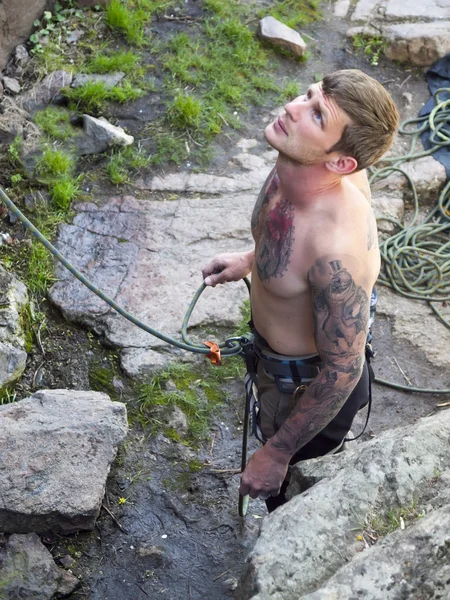 The man with the tattoos is engaged in rock climbing.